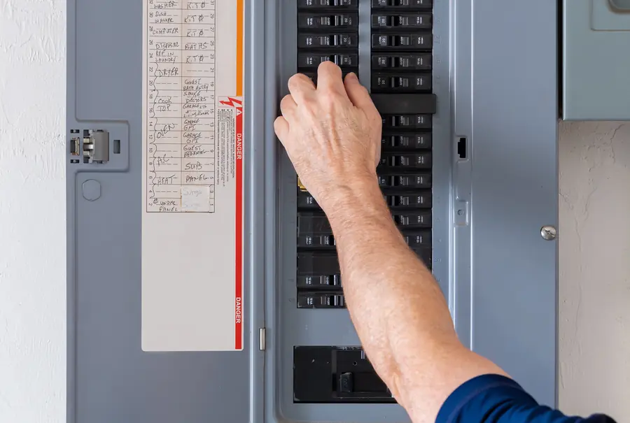 A hand at the breakers of a residential electrical panel