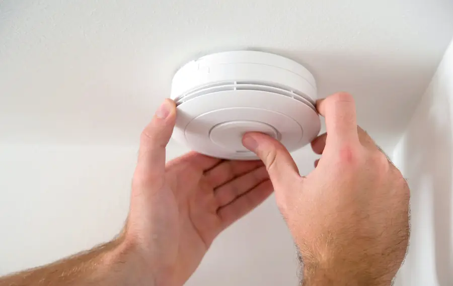 Hands fitting a smoke detector to a ceiling
